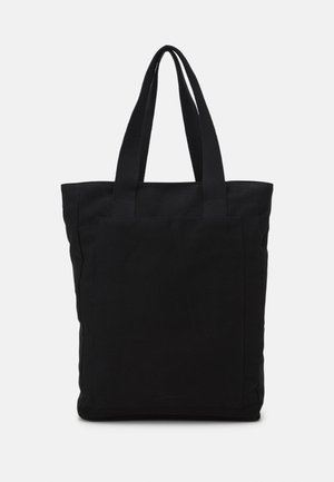 Sac fourre-tout en tissu noir avec de longues poignées et une grande poche avant, présenté sur un fond blanc uni.
