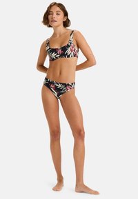 Květinový bikini set s černým podkladem a živými růžovými a zelenými vzory. Horní část má široké ramínka; spodní část je v klasickém střihu.