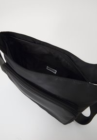 Borsa a spalla sintetica nera con scomparto principale con zip e tasca esterna. Presenta una tracolla in tessuto e un interno foderato.