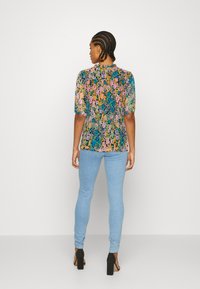 Blusa de mangas curtas, floral e em cores vibrantes, com um corte solto. Combinada com uns jeans skinny azuis claros e sapatos de salto alto pretos.