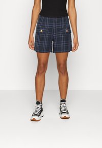 Navy plaid shorts featuring two front pockets with gold buttons, paired with black high-top sneakers. Smooth fabric, tailored fit, and casual design.