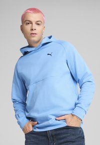 Sudadera azul claro hecha de tejido suave, con un detalle de costura en el frente y el logo negro de Puma en el pecho. Cuenta con un capucho ajustable y mangas largas.