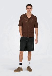 Brown short-sleeve, button-up shirt with a textured pattern, paired with black shorts and beige shoes. White socks with black stripes visible.