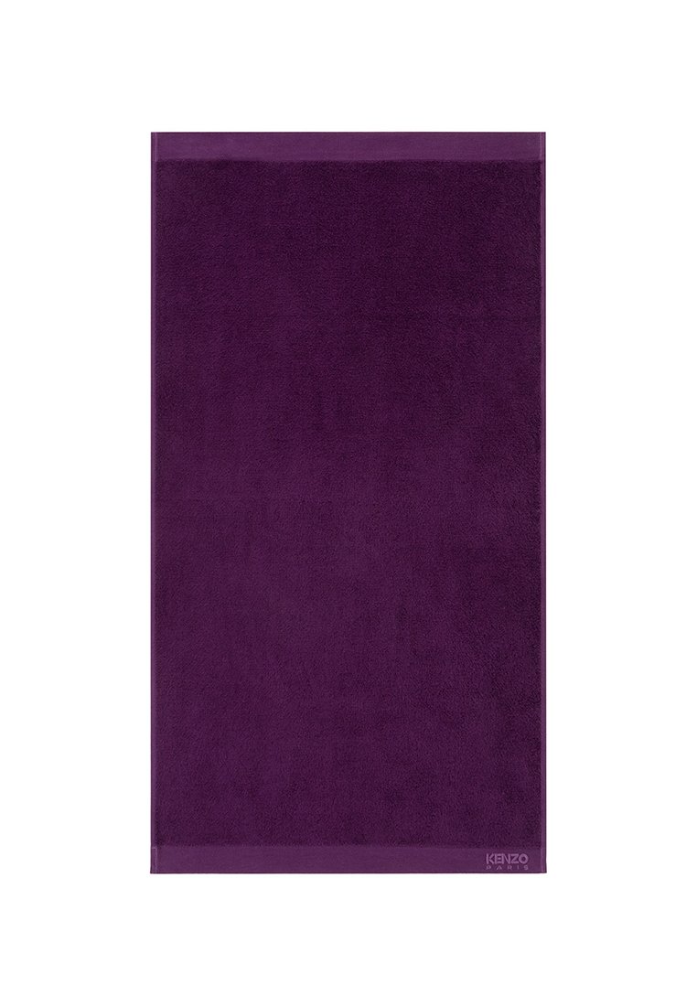 Toalla de felpa morada con una textura suave, bordeada por un borde liso. Presenta un pequeño logotipo en la esquina inferior.