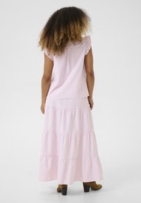 Haut sans manches rayé rose avec des manches volantées, associé à une jupe maxi à étages, dotée d'une taille ajustée et d'un tissu fluide. Bottes à talons marron.