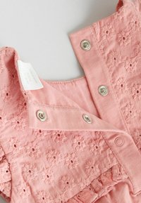 Rózsaszín pamut body virágos hímzéssel, patentos záródással és puha tapintású anyagból. A címkén a "NEXT" felirat és ápolási utasítások találhatók.