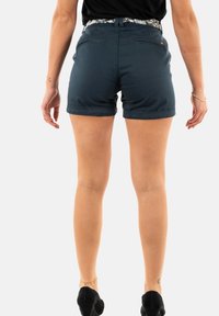 Shorts bleu foncé en mélange de coton, présentant une coupe ajustée, un ourlet roulé et des poches arrière. Portés avec une ceinture à motifs.