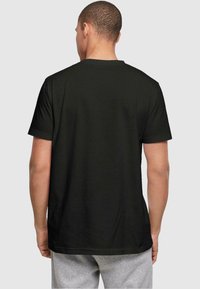 Svart bomullst-skjorte med korte ermer, rund hals og rett kant, brukt sammen med grå joggebukser; glatt tekstur uten synlige logoer.