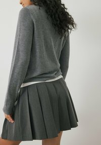 Grau gestrickter Pullover mit rundem Halsausschnitt, kombiniert mit einem grauen plissierten Rock. Der Pullover hat einen hellfarbenen Bund.