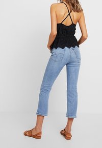 Czarny bezrękawnik z koronkowym dołem, połączony z jasnoniebieskimi, krótkimi dżinsami i brązowymi sandałami. Z tyłu znajduje się krzyżujące się ramiączka.