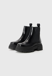 Bottines Chelsea en cuir noir avec des panneaux latéraux élastiques et des languettes, dotées d'une semelle en caoutchouc épaisse et d'une finition lisse et brillante.