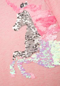 Rosa Stoff mit einem Pailletten-Einhorn-Muster. Die Mähne des Einhorns vereint pinke, silberne und schillernde Pailletten mit einer strukturierten Oberfläche.