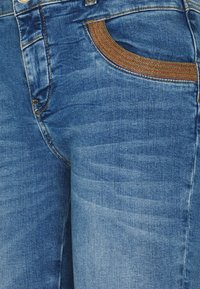 Jeans de mezclilla con un lavado azul intermedio, que presentan un ajuste slim, detalles de desvanecimiento y un acento texturizado de cinturón multicolor en la zona de los bolsillos.