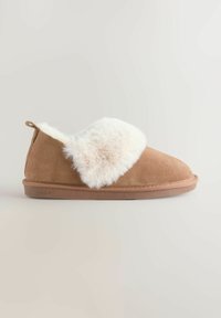 Brown suede slipper with cream-colored fluffy lining and cuff, flat sole, and pull tab on heel.