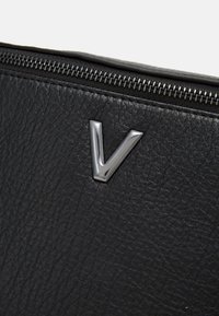 Sac en cuir noir avec une surface texturée, fermeture zippée argentée et accent métallique en forme de 'V'.
