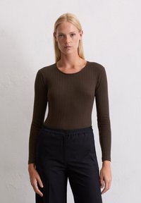 Bruin geribde longsleeve top met een ronde halslijn, gecombineerd met zwarte pantalons met elastische taille. De stof lijkt rekbaar en aansluitend.