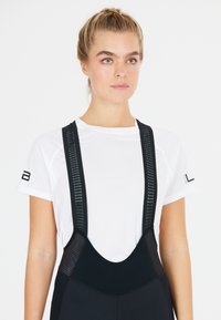 Schwarze Radshorts mit Netzträgern, kombiniert mit einem weißen, kurzärmligen, feuchtigkeitsregulierenden Sportoberteil. Strukturiertem Gewebe und enganliegendem Design.