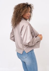 Bomberjack in lichtbeige satin, met een fitted tailleband, geribbelde manchetten en een zijritsdetail. Gekocht bij een lichte blauwe spijkerbroek.