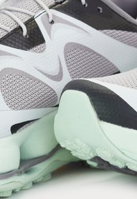 Des chaussures de sport grises et noires avec une tige en maille, présentant une semelle mint verte rembourrée et de multiples motifs de semelle pour une traction optimale.