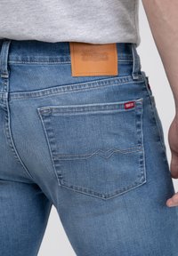 Jeans de mezclilla azul desgastados con un parche de cuero etiquetado "BIG STAR" en la cintura y una pequeña etiqueta de marca roja en el bolsillo trasero.