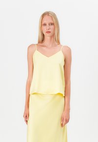 Camisón de satén amarillo con tirantes finos y un diseño de escote en V, combinado con una falda midi a juego. Textura suave y silueta fluida.