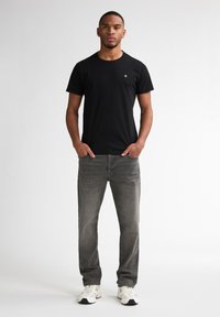 Tricou negru din bumbac, cu mâneci scurte și un mic logo pe piept, asortat cu blugi din denim gri și adidași albi.