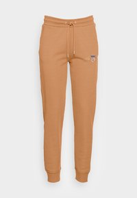 Beiga sweatpants i mjukt tyg, med dragsko i midjan, ribbade muddar och en liten broderad logotyp på vänster lår.