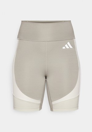 Beige idrettsshorts med høy midje, laget av stretchy stoff. Har hvite sidestykker og et Adidas-logo på øvre høyre side.