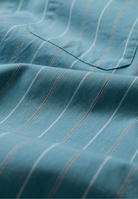 Katoenen stof in een gestructureerd blauw met witte en bruine verticale strepen. Heeft een borstzak en een zachte val.