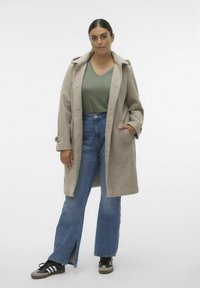 Abrigo de lana beige con capucha, con grandes botones y bolsillos laterales, llevado sobre una blusa verde y jeans de mezclilla acampanados con una abertura.