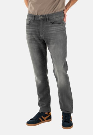 Jeans in denim grigio con taglio dritto, caratterizzati da un lavaggio sbiadito, cinque tasche e un delicato effetto di whiskering. Abbinati a sneakers blu navy con dettagli arancioni.