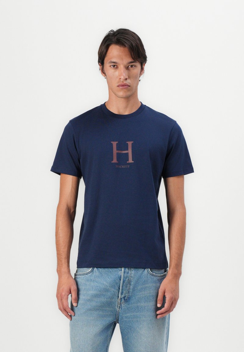 Námornícky modré bavlnené tričko s krátkymi rukávmi, s veľkým burgundským logom "H" v strede a s nápisom "Hackett" pod ním. Klasický strih.