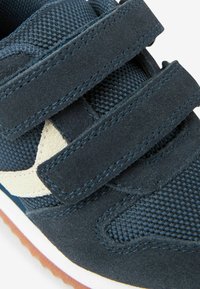 Granatowe sneakersy wykonane z zamszu i siateczki, z rzepami, wzorowanym materiałem tekstylnym oraz gumową podeszwą z beżowym akcentem.