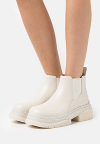 Botas de tobillo de piel blanca con paneles laterales elásticos, punta redondeada y suela gruesa y texturizada. Acabado suave con un mínimo de detalles.