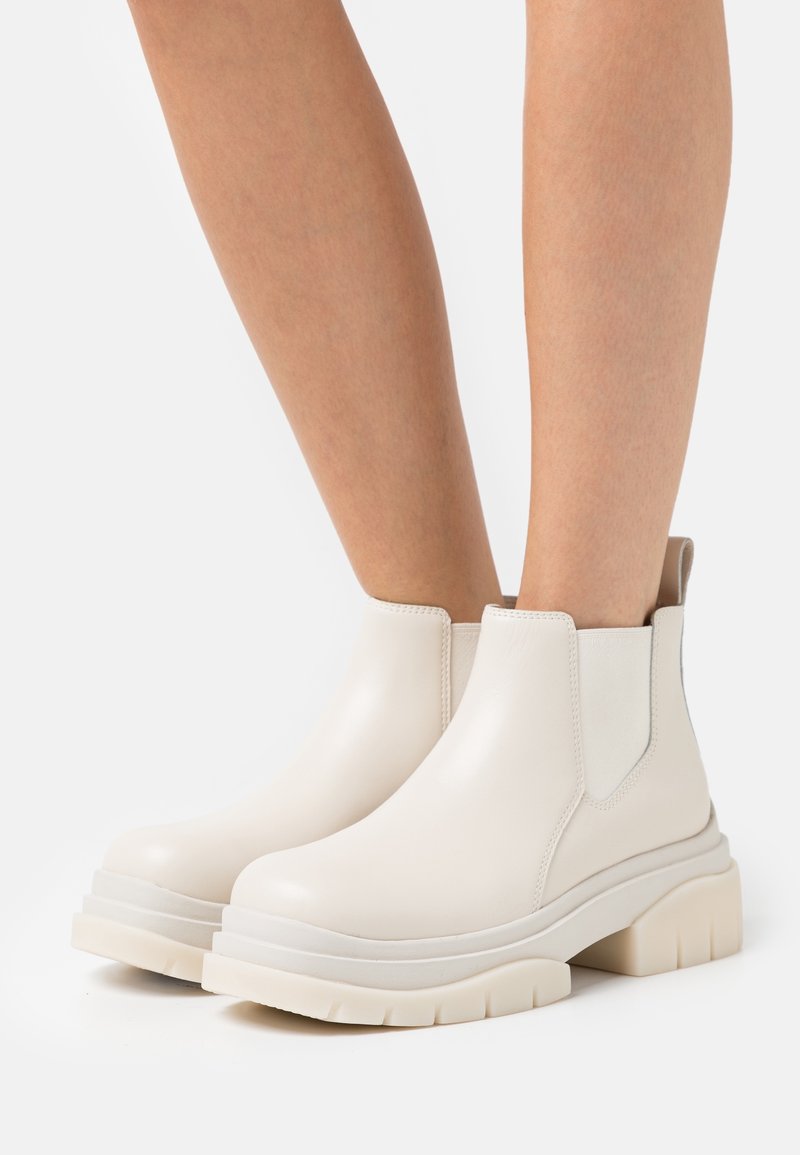 Botas de tobillo de piel blanca con paneles laterales elásticos, punta redondeada y suela gruesa y texturizada. Acabado suave con un mínimo de detalles.