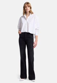 Vit avskuren skjorta med knappar och långa ärmar, matchad med svarta högmidjade utsvängda jeans och vita pointy-toed skor. Minimal detaljering.