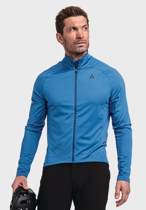 Blaue Sportjacke mit hohem Kragen, durchgehendem Reißverschluss und langen Ärmeln. Glatte Textur mit schwarzem Logo auf der Brust. Schwarze Shorts und Helm in der Hand.