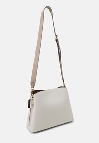 Bílá kožená kabelka přes rameno se strukturovaným tvarem, béžovým popruhem a zlatými kovovými akcenty, s hladkým povrchem a minimalistickým designem.