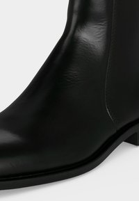 Bottine en cuir noir poli avec un petit talon et un bout arrondi lisse, montrée en gros plan.