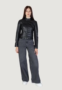 Svart konstläderjacka med en figursydd design, tryckknappsstängning och långa ärmar, ihop med lösa mörkgrå jeans och vita skor.