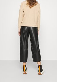 Svarta fusk läder culotter med vid benringning, i kombination med en beige stickad tröja och svarta hög-top sneakers med orange detaljer.