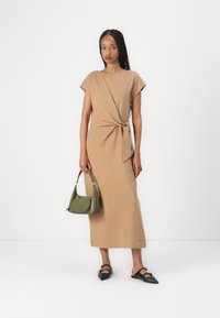 Beige midi ruha rövid ujjakkal, csomózott derékrésszel, zöld táskával és fekete hegyes orrú cipővel párosítva. Sima szövettextúra.