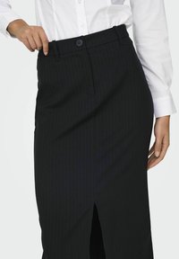Zwarte pinstripe rok met een voorsplit, voorzien van een aansluitende taille en een enkele knoopsluiting. Gemaakt van glad, gestructureerd materiaal.