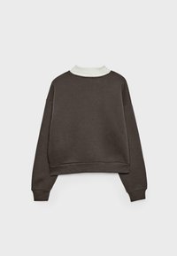 Mørkebrun langærmet cropped sweatshirt med ribstrikkede manchetter og kant, lagdelt over en hvid top med høj hals, vist bagfra.