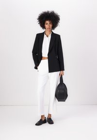 Blazer preto de dois sentidos, blusa branca cropped, calças brancas de perna larga, sapatos pretos de loafers e uma bolsa estruturada preta. Texturas suaves, formas modernas.