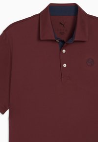 Bordeaux polo shirt med krave, med en marineblå inderside og et lille sort Puma-logo på venstre side. Tre knapper synlige.