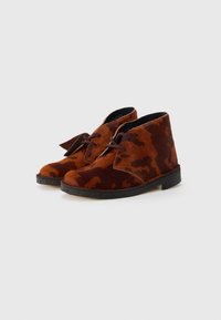 Stivali ankle in pelle marrone con un design testurizzato e variegato. Presentano lacci marroni e una suola in gomma nera. Finitura liscia con un aspetto morbido.