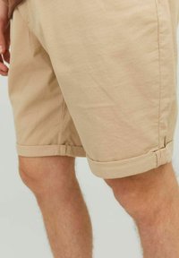 Shorts beiges en tissu texturé avec des ourlets retroussés, présentant une coupe droite et un design décontracté, mettant en valeur la partie supérieure de la jambe.