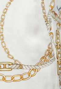 Valge kangas, millel on ahela ja köie muster kuldsetes ja beežides toonides, esitades sujuva tekstuuri ja detailsete lülide kontuuridega.