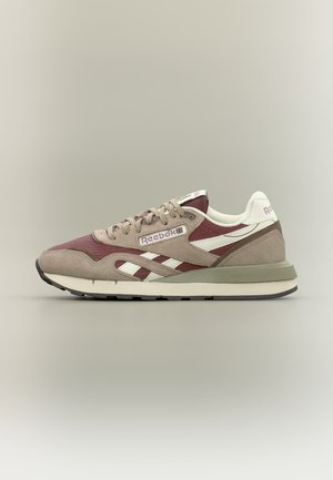 Vista lateral de una zapatilla Reebok color burdeos y beige con rayas blancas y cordones beige sobre un fondo liso.